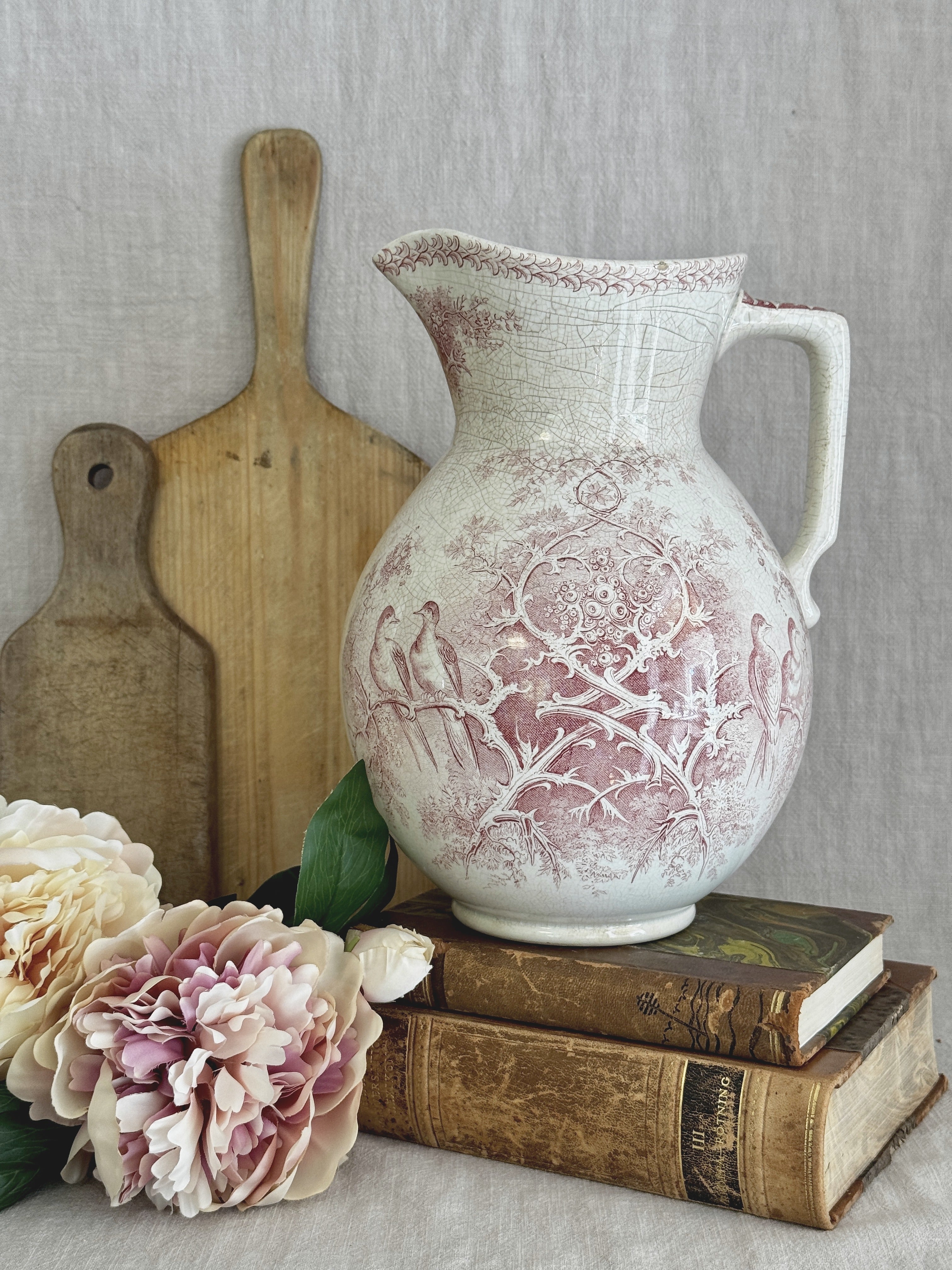 Antique French Sarreguemines Colomba jug in red transferware, styled on antique books beside a wooden bread board