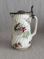 Front view of the ribbed faience jug with pewter lid and polychrome floral decoration