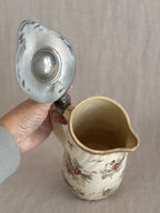 The pewter lid held open, showing the cream glazed interior and spout