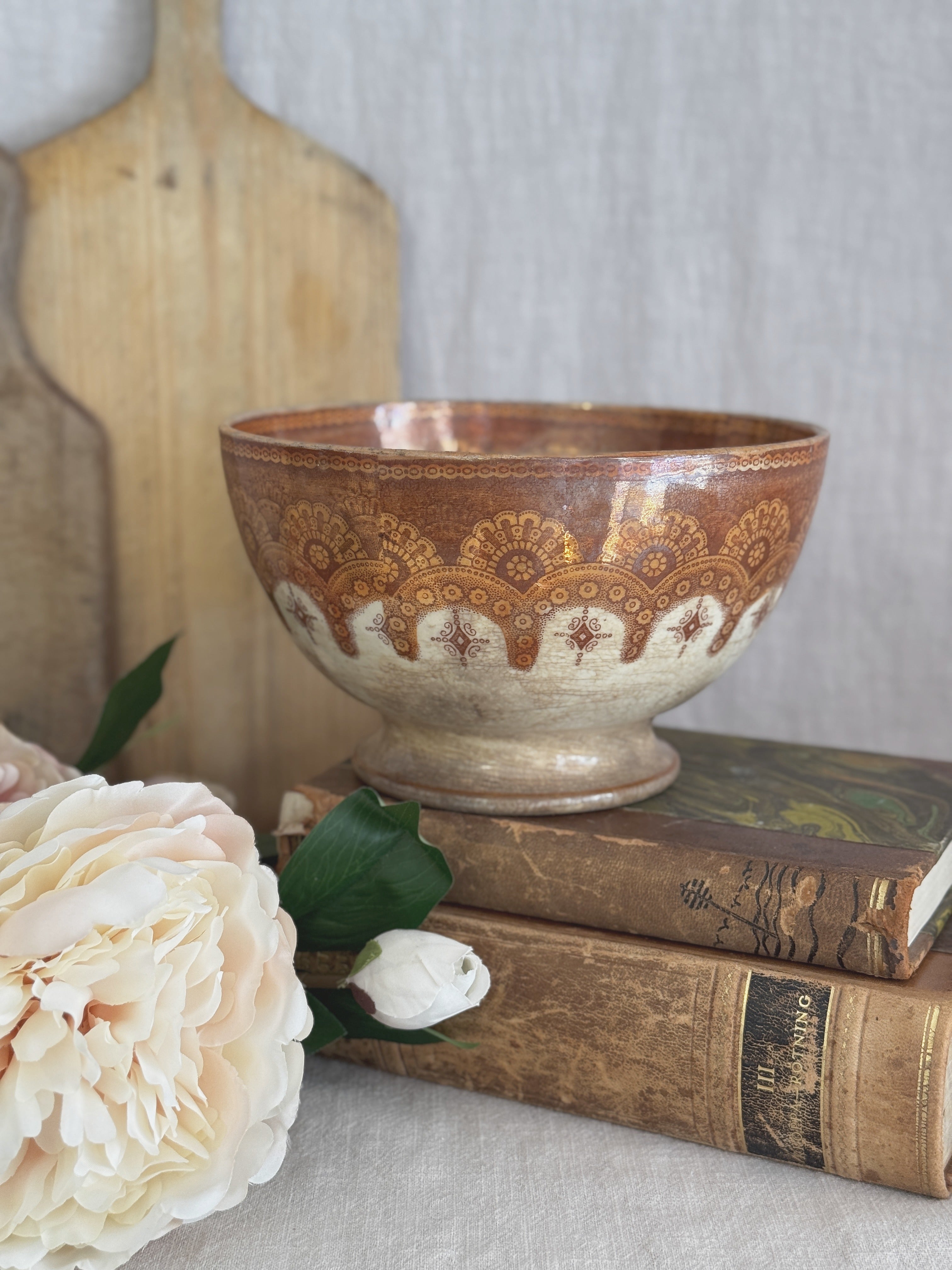 Large copper lustre footed bowl styled on antique books with a peony and a wooden bread board
