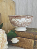 Brown transferware café au lait bowl with safari animals, styled on antique books with a peony and a bread board