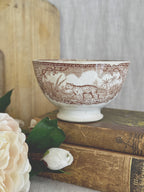 Brown transferware café au lait bowl with safari animals, styled on antique books with a peony and a bread board