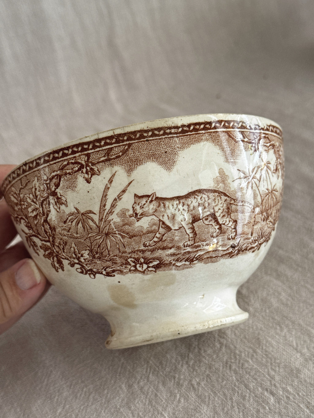 Side view of the footed bowl showing the brown transfer band of animals on cream earthenware