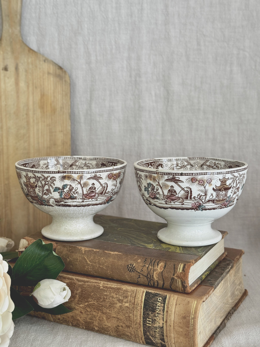 The two footed bowls seen together on antique books beside a wooden bread board