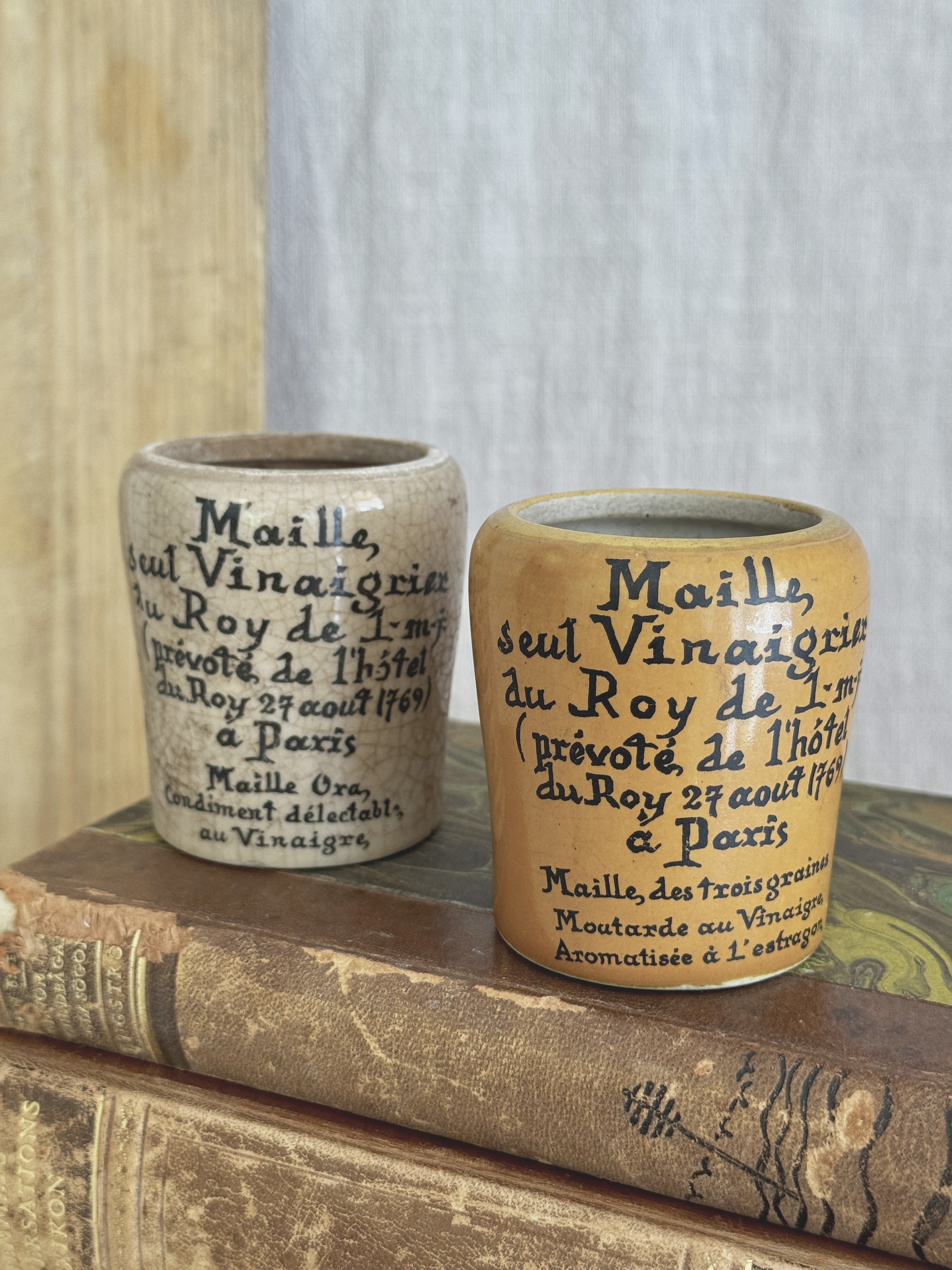 Pair of French Maille stoneware mustard pots, one ochre and one cream, standing on antique books