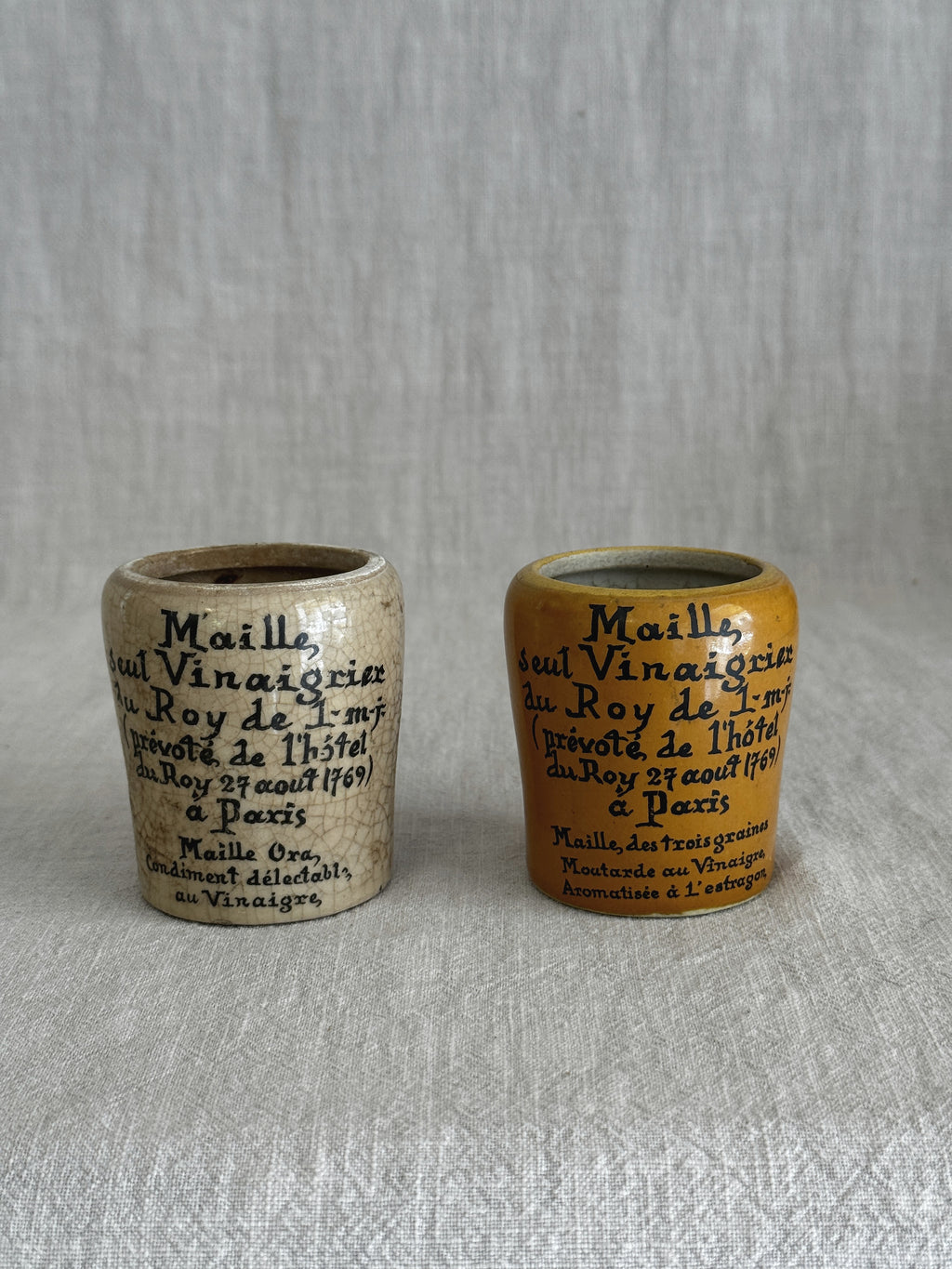 Both Maille mustard pots seen side by side showing the printed Paris text on each