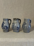 Three German salt-glazed stoneware jugs standing in a row on linen