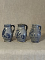 Three German salt-glazed stoneware jugs standing in a row on linen