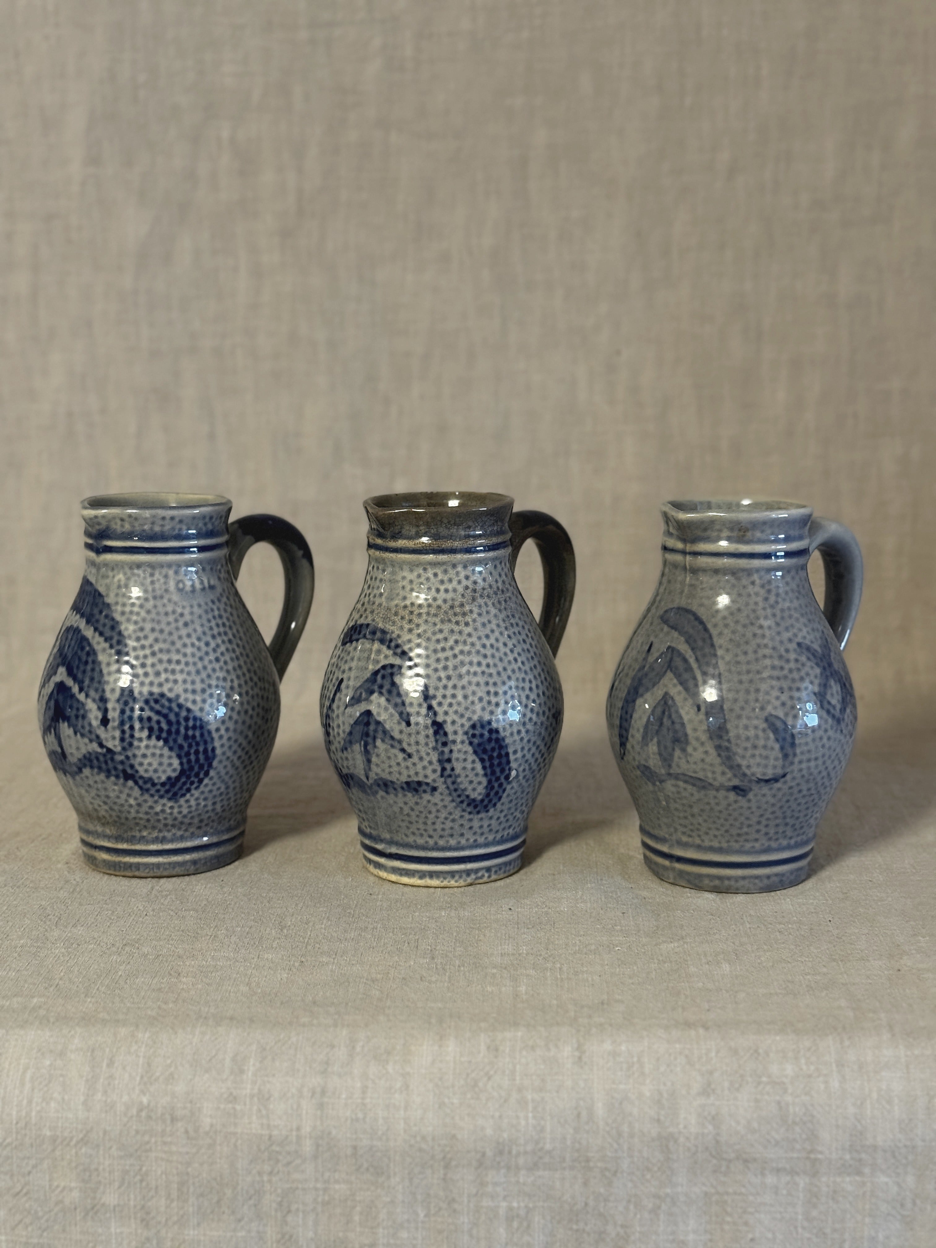 Three German salt-glazed stoneware jugs standing in a row on linen