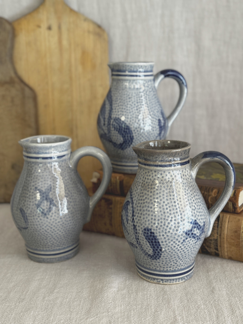 The three cobalt and grey stoneware jugs grouped on a bread board with antique books