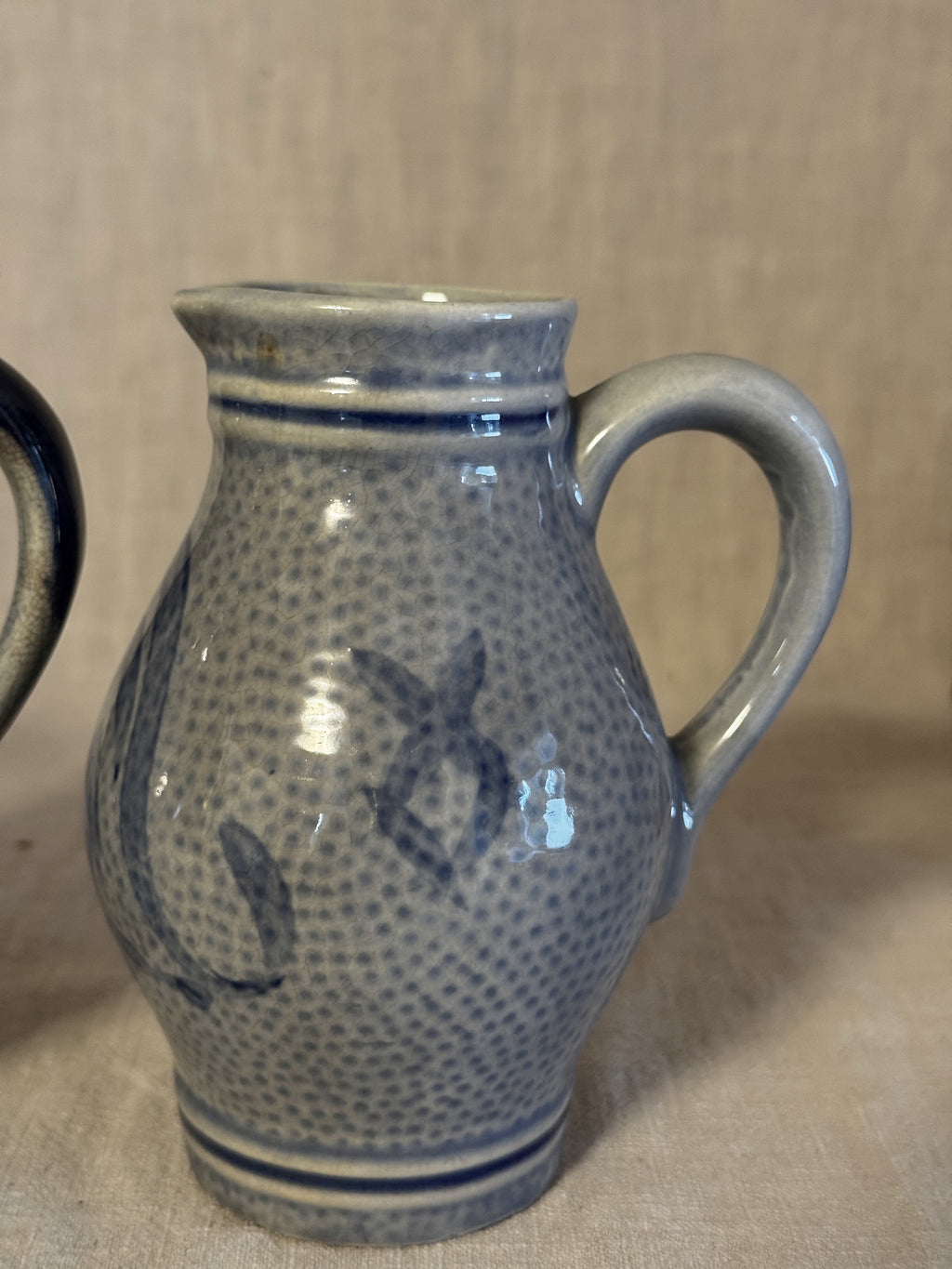 Close view of one jug showing the pebbled salt-glazed surface and cobalt blue motif
