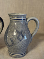 Close view of one jug showing the pebbled salt-glazed surface and cobalt blue motif