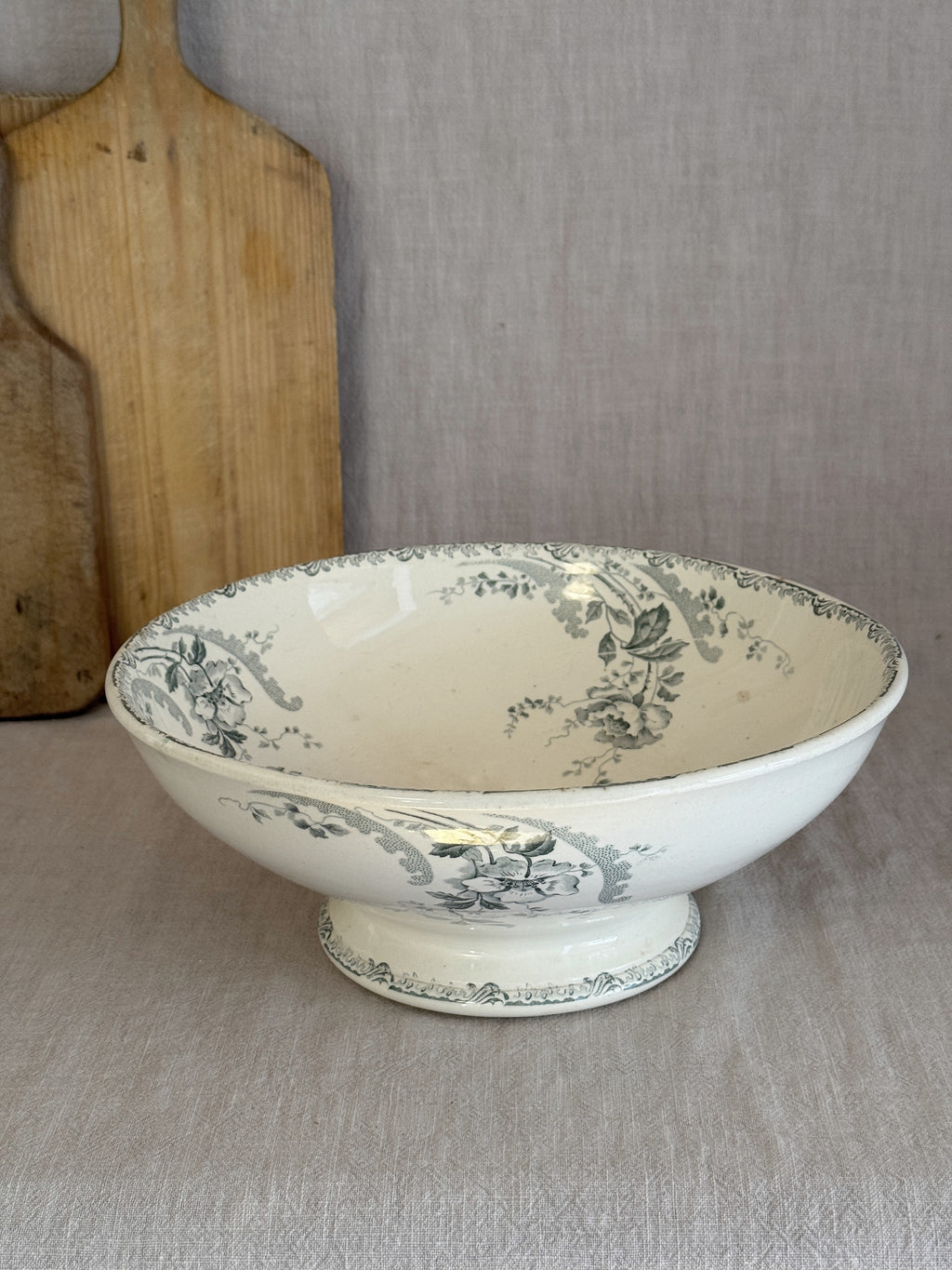 Antique Choisy-le-Roi footed salad bowl seen from the side on a linen cloth, with a wooden board behind