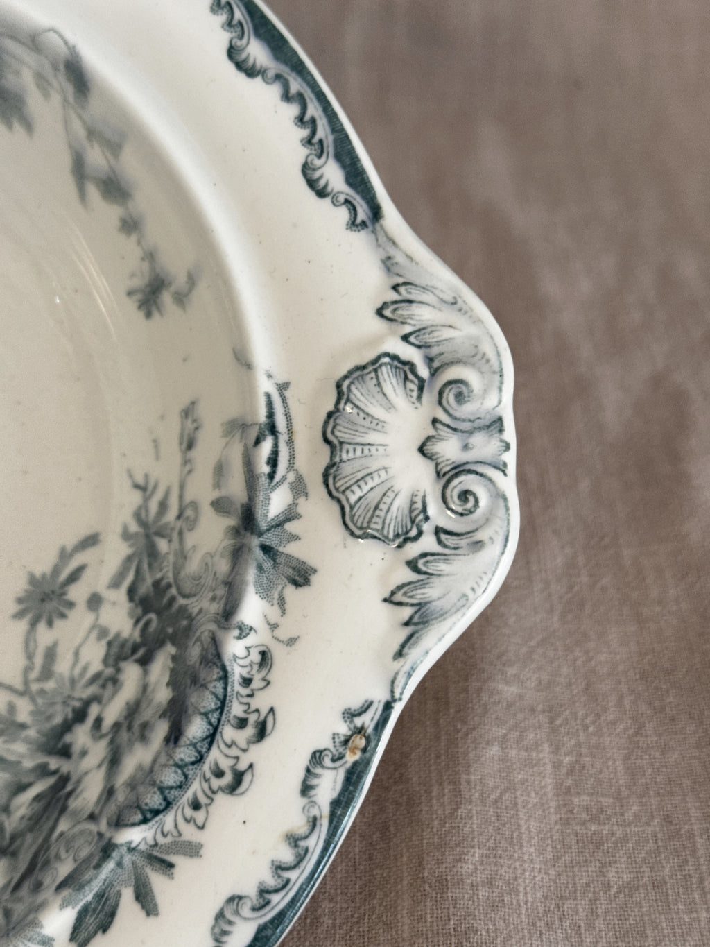 Close view of a moulded shell handle and the teal rocaille border on the earthenware rim