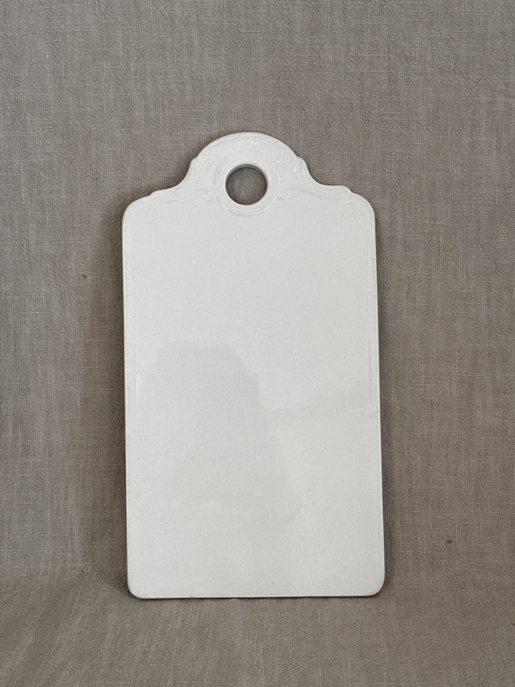 Antique white faience board with moulded rococo shell relief and hanging hole, glazed front, on linen