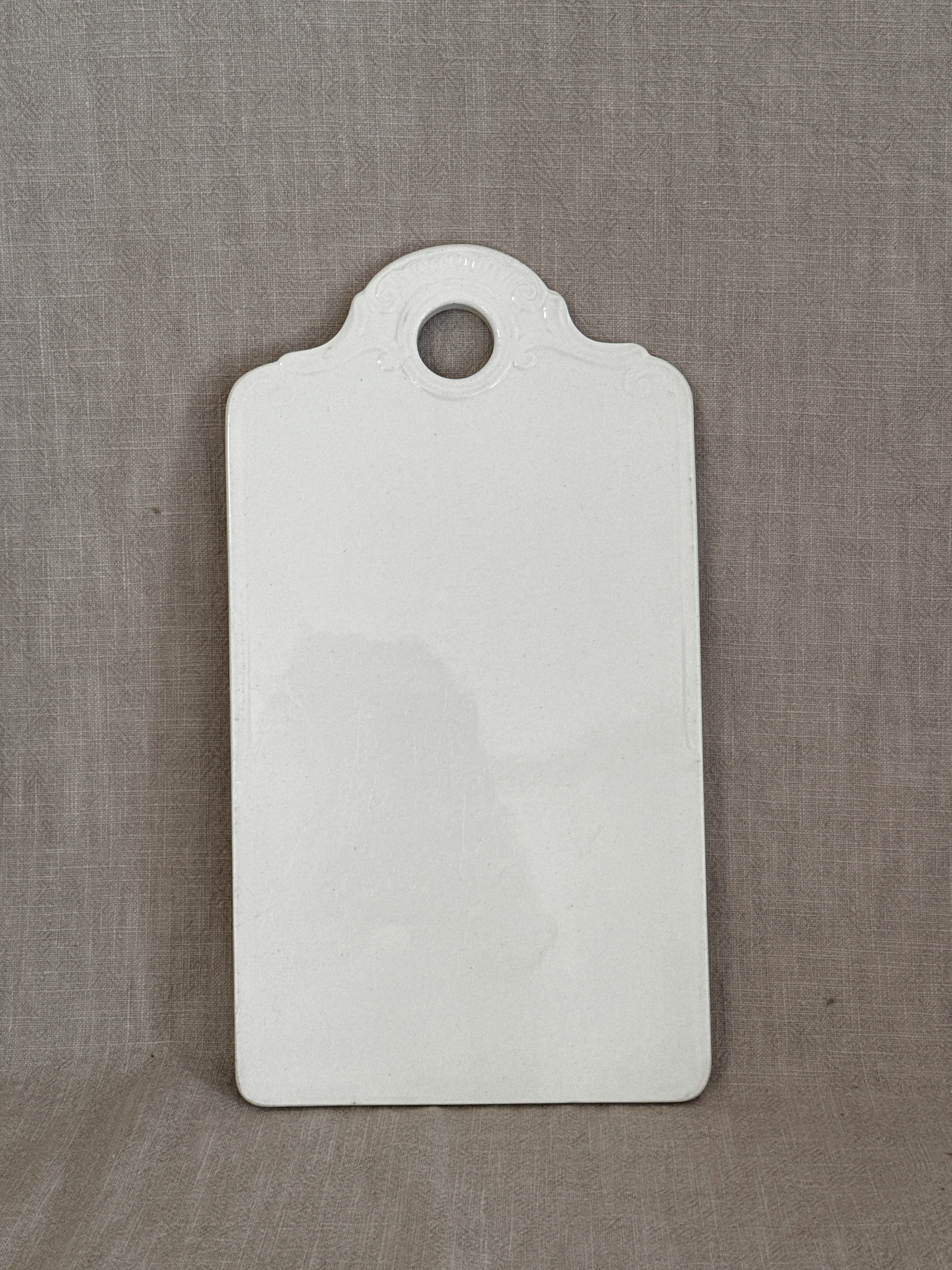 Antique white faience board with moulded rococo shell relief and hanging hole, glazed front, on linen