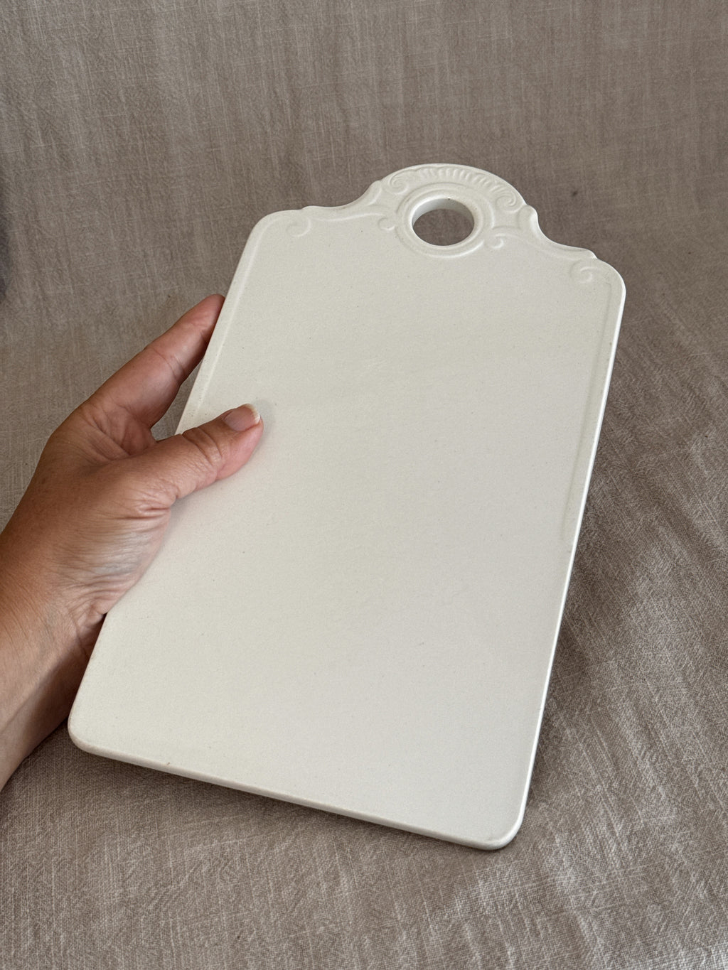 Matt bisque reverse of the white faience board, held in a hand for scale