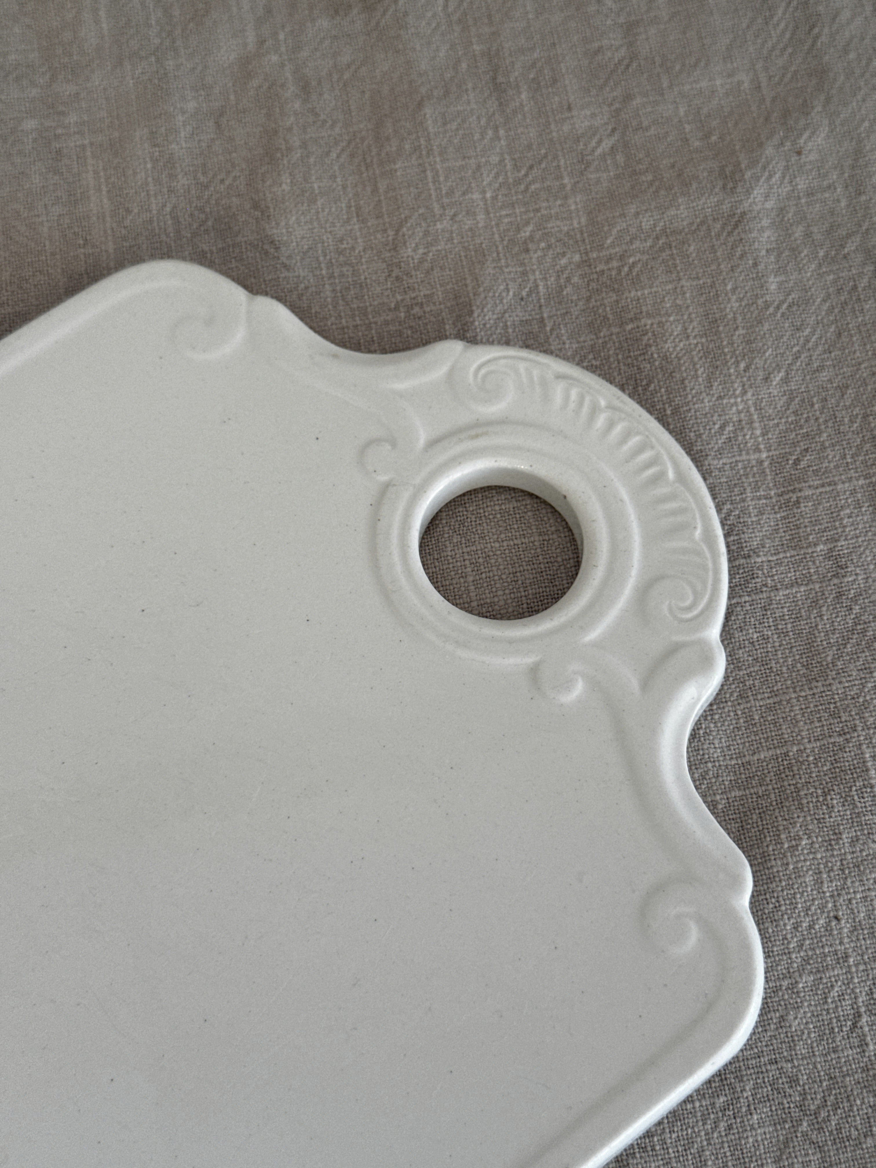Close-up of the moulded shell and C-scroll relief around the hanging hole of the faience board
