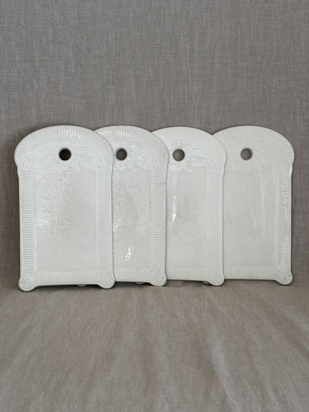 Four identical vintage Belgian white faience boards with fluted relief frames, standing in a row