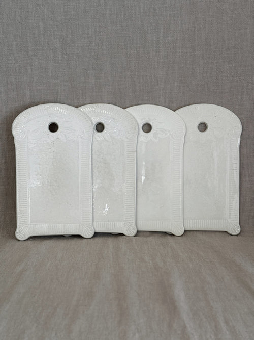 Four identical vintage Belgian white faience boards with fluted relief frames, standing in a row