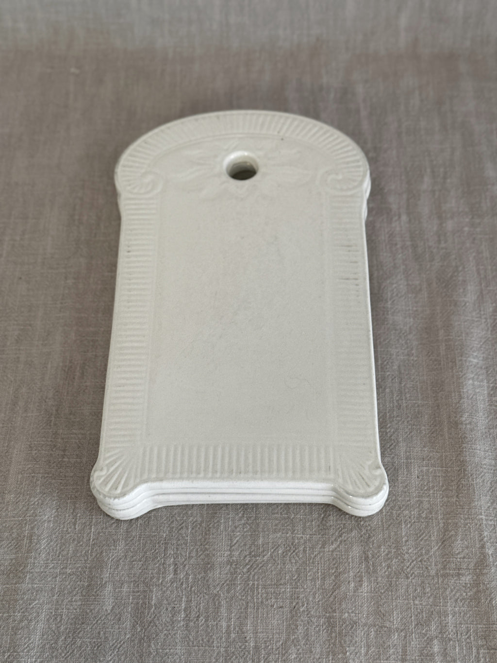 Single white faience board seen from above, fluted frame with fan corners and hanging hole