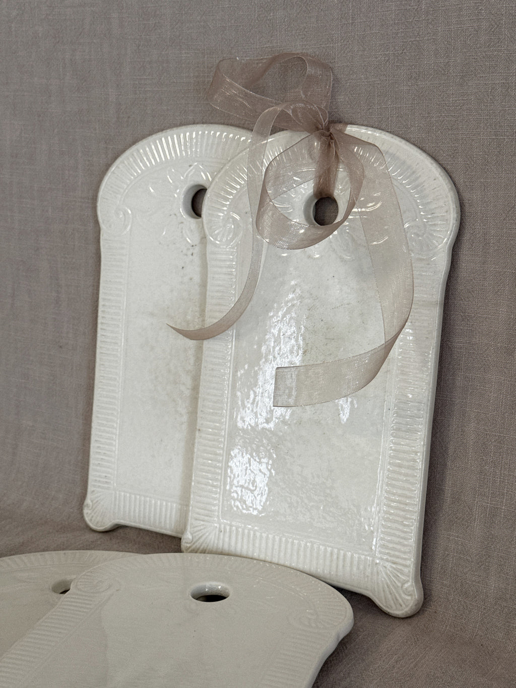 Two white faience boards leaning together with a sheer ribbon tied through the hanging hole