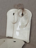 Two white faience boards leaning together with a sheer ribbon tied through the hanging hole