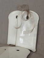 Two white faience boards leaning together with a sheer ribbon tied through the hanging hole