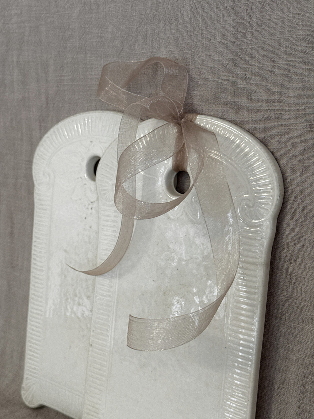 Close-up of the glazed face of a white faience board with a ribbon through the hanging hole