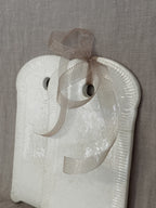 Close-up of the glazed face of a white faience board with a ribbon through the hanging hole