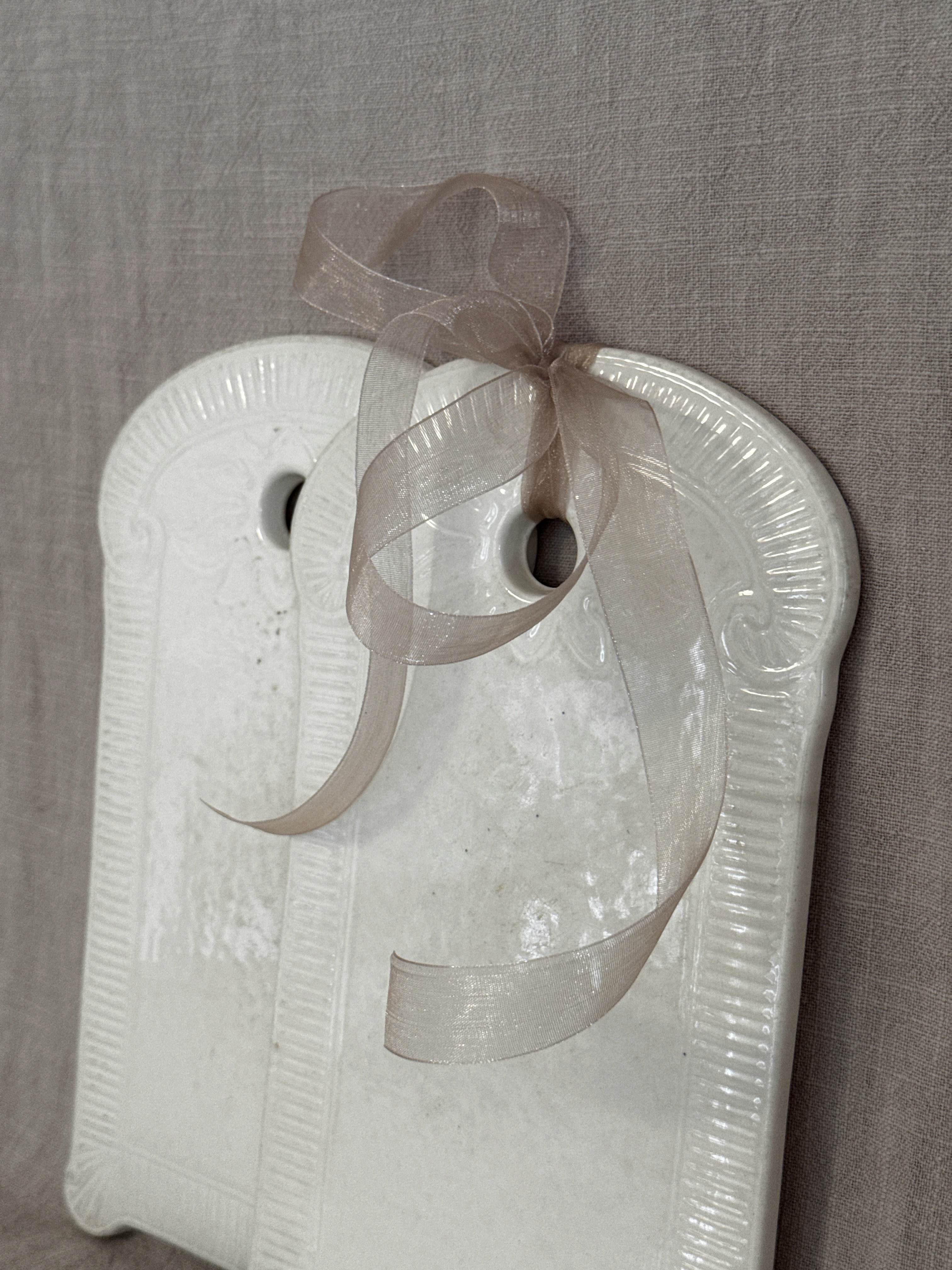 Close-up of the glazed face of a white faience board with a ribbon through the hanging hole
