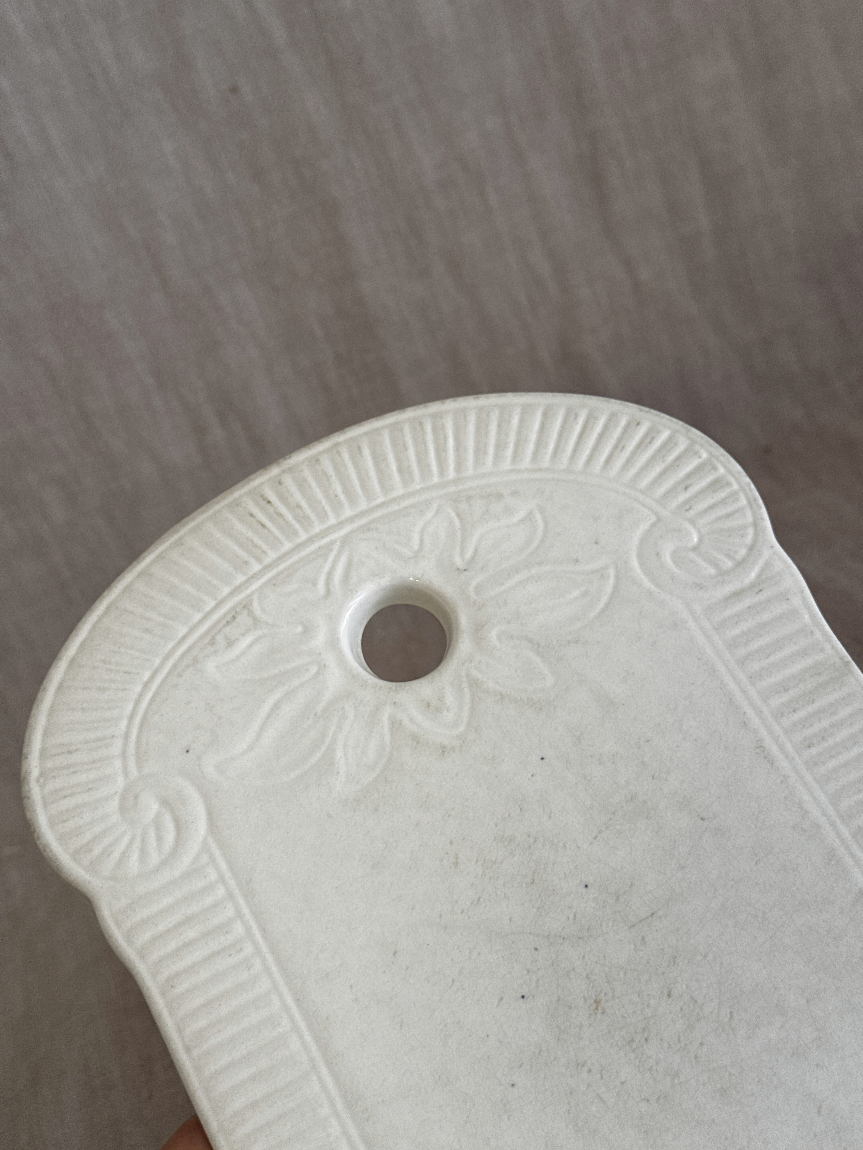 Detail of the leaf palmette relief around the hanging hole on a white faience board