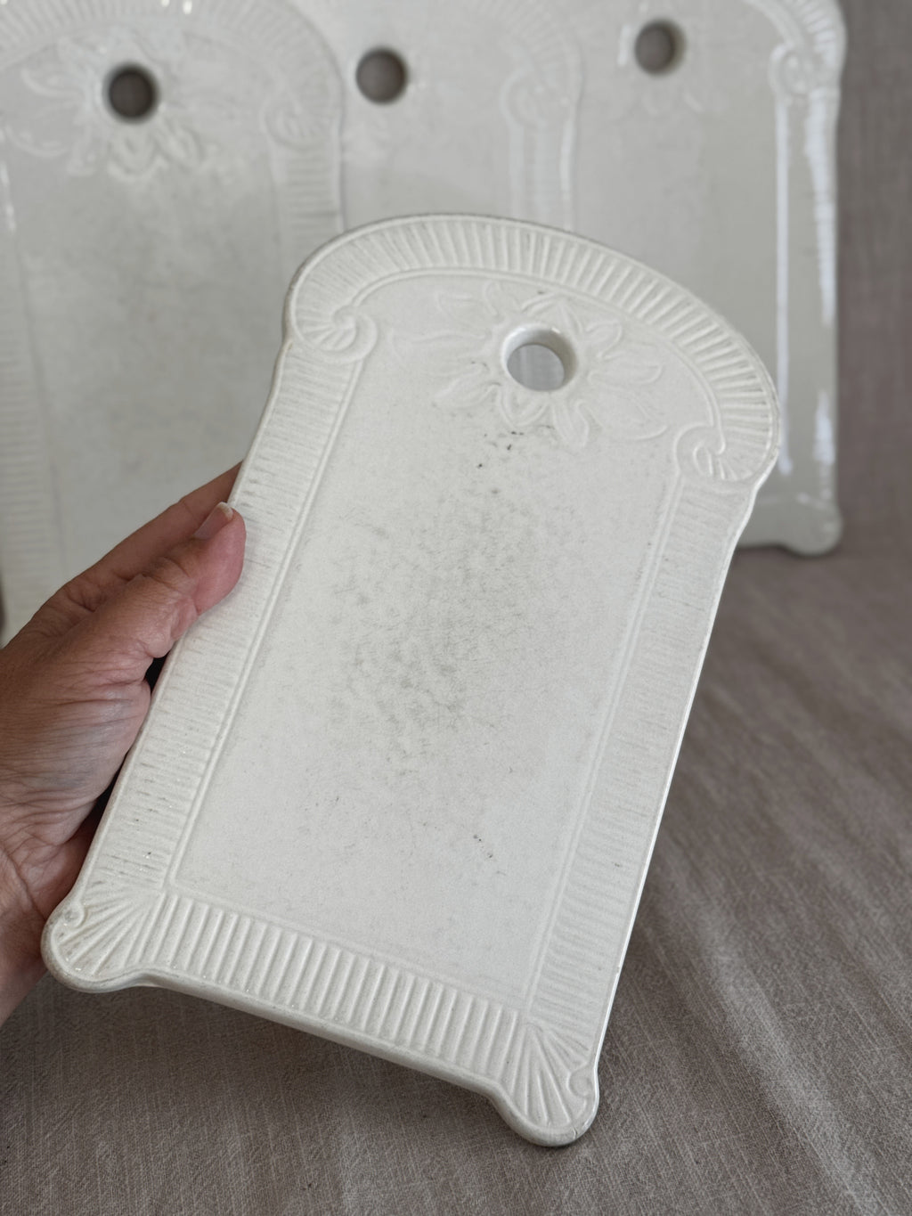 White faience board held in a hand, the other three standing behind on linen