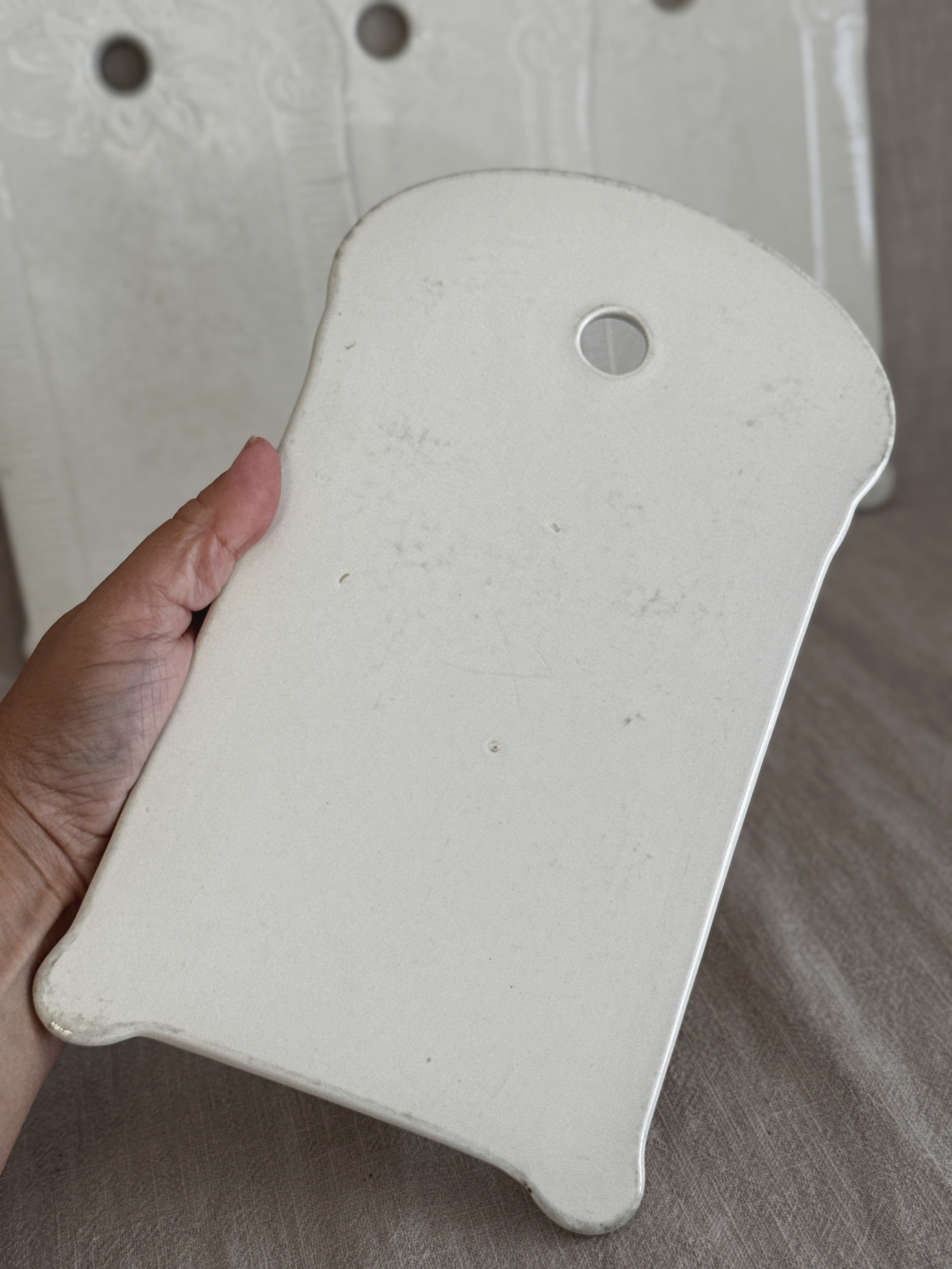 Unglazed reverse of a white faience board held in a hand, showing the matt earthenware body