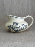 Antique Gien faience jug in cream with a blue-grey printed trumpet flower spray, a wide flat spout and a bamboo-shaped handle, on a linen backdrop