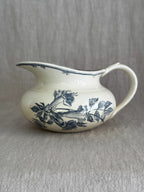 Antique Gien faience jug in cream with a blue-grey printed trumpet flower spray, a wide flat spout and a bamboo-shaped handle, on a linen backdrop