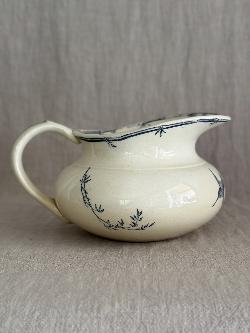 Side profile of the low wide jug showing the flared spout, the hand-painted bamboo border at the rim and the tall curved handle