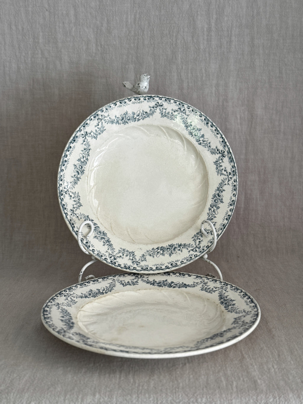 Pair of antique French Longwy faience plates with teal ribbon and garland borders, one upright on a stand and one lying flat