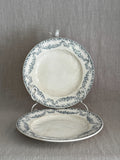 Pair of antique French Longwy faience plates with teal ribbon and garland borders, one upright on a stand and one lying flat
