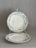 Pair of antique French Longwy faience plates with teal ribbon and garland borders, one upright on a stand and one lying flat