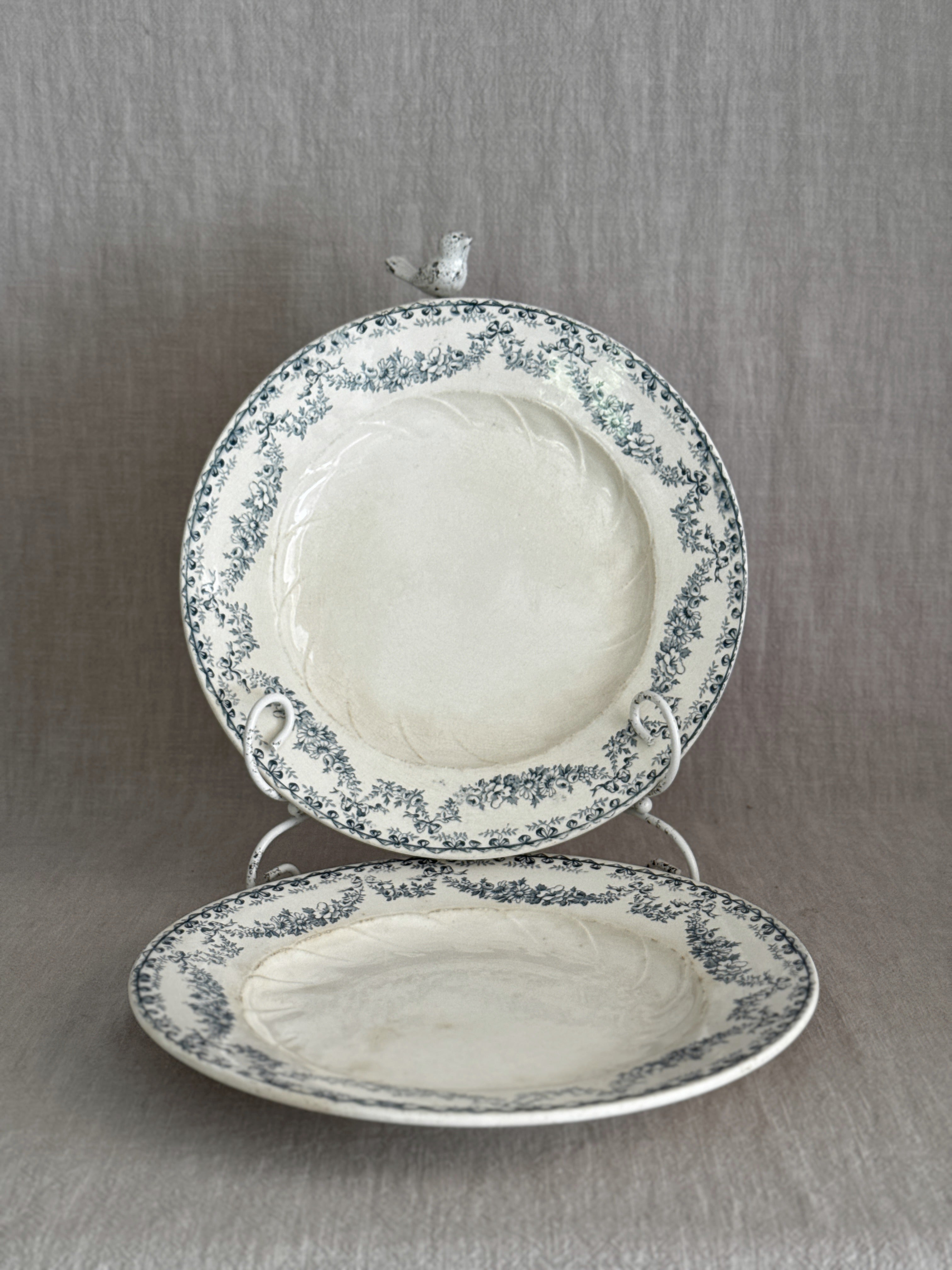 Pair of antique French Longwy faience plates with teal ribbon and garland borders, one upright on a stand and one lying flat