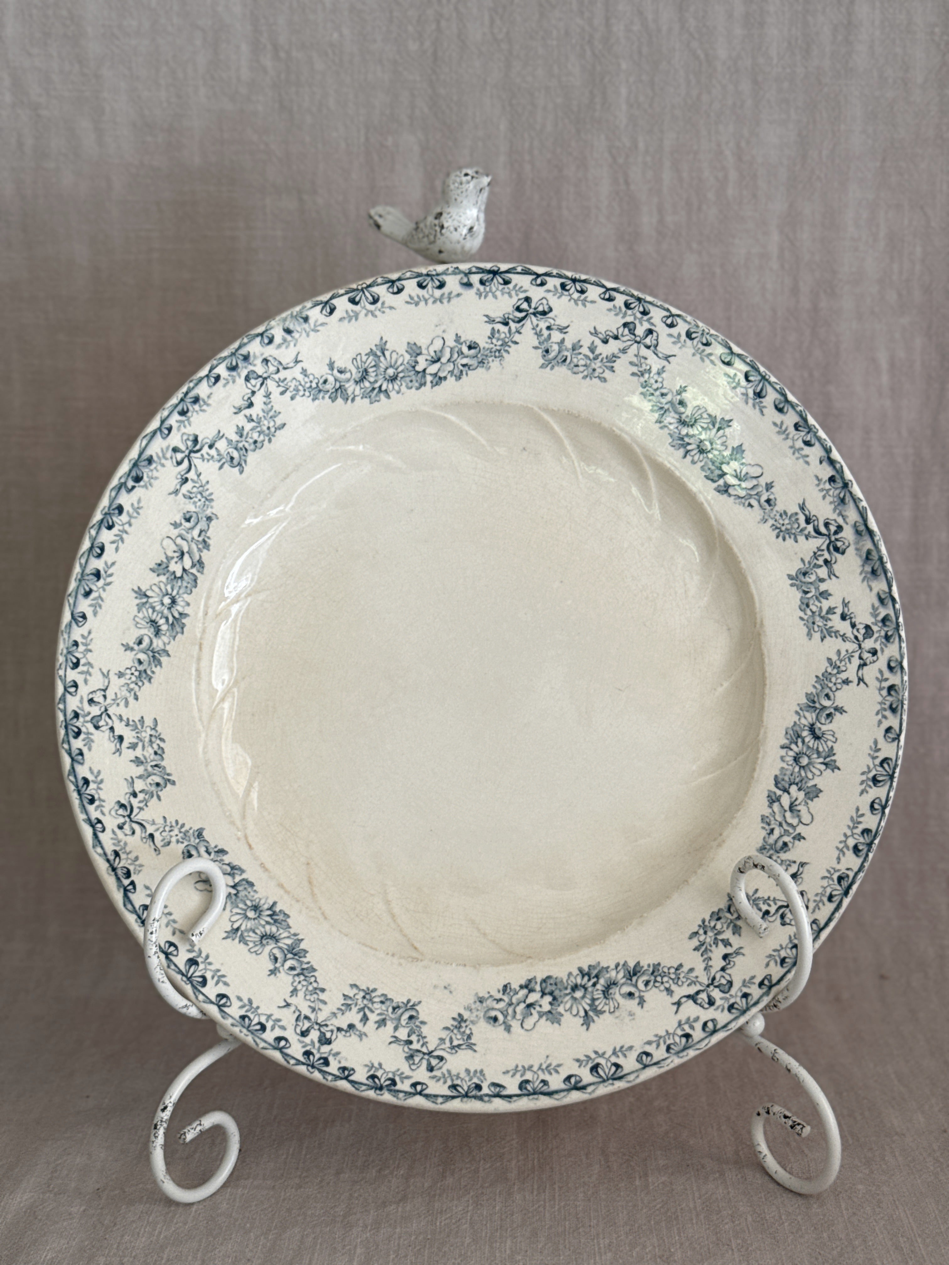 A single Longwy plate upright on a white stand, showing the full teal garland border and the moulded swirl in the well