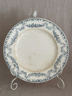 Close view of a Longwy plate face with printed bows, flower swags and soft amber staining across the well