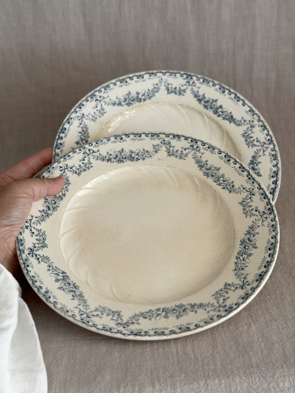 The pair of Longwy plates held in one hand, the two teal garland borders side by side