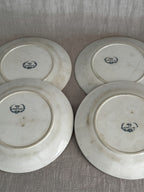 Reverses of all four plates side by side on linen, each carrying the blue Badonviller wreath mark and an impressed mould number