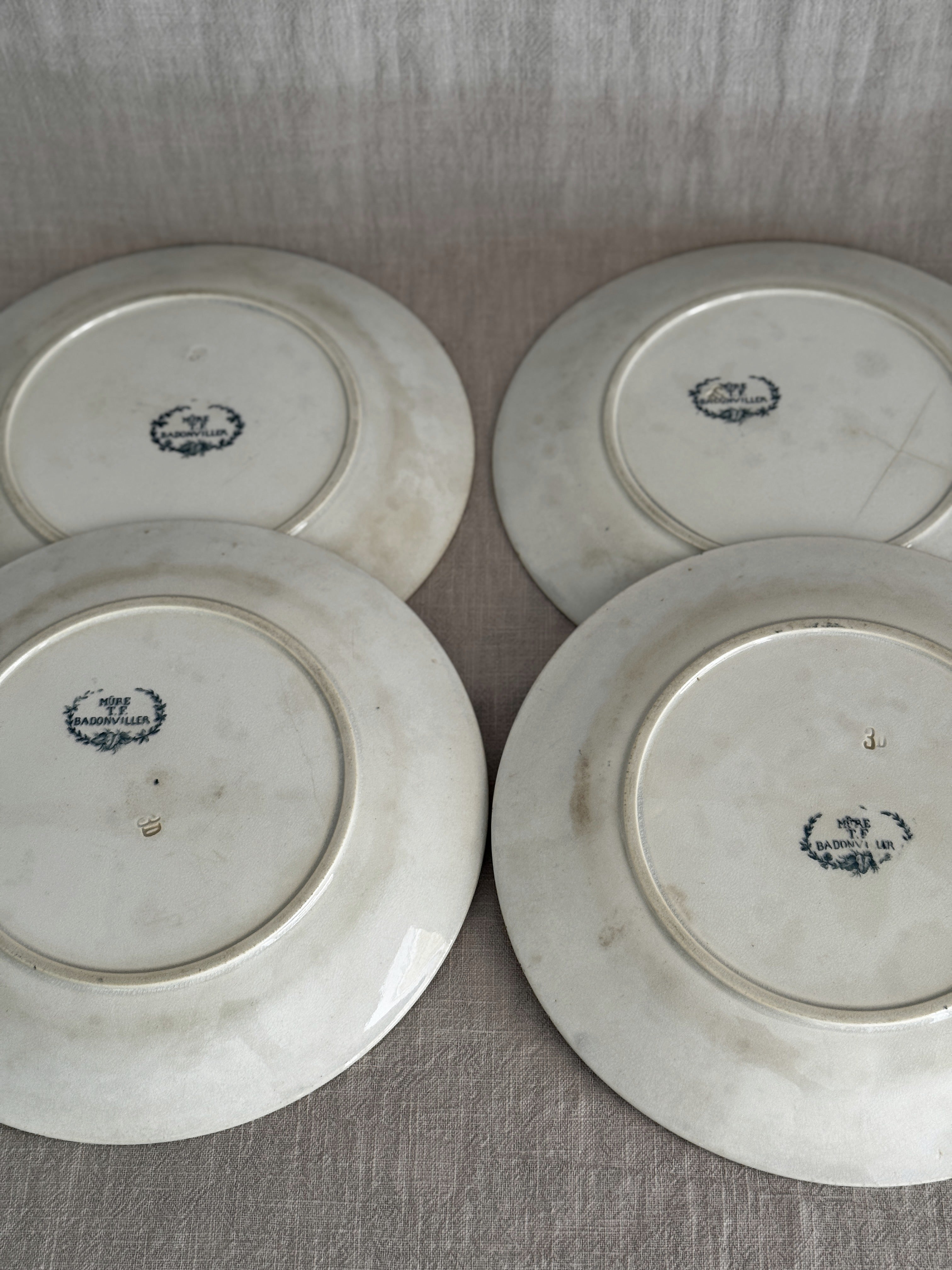 Reverses of all four plates side by side on linen, each carrying the blue Badonviller wreath mark and an impressed mould number