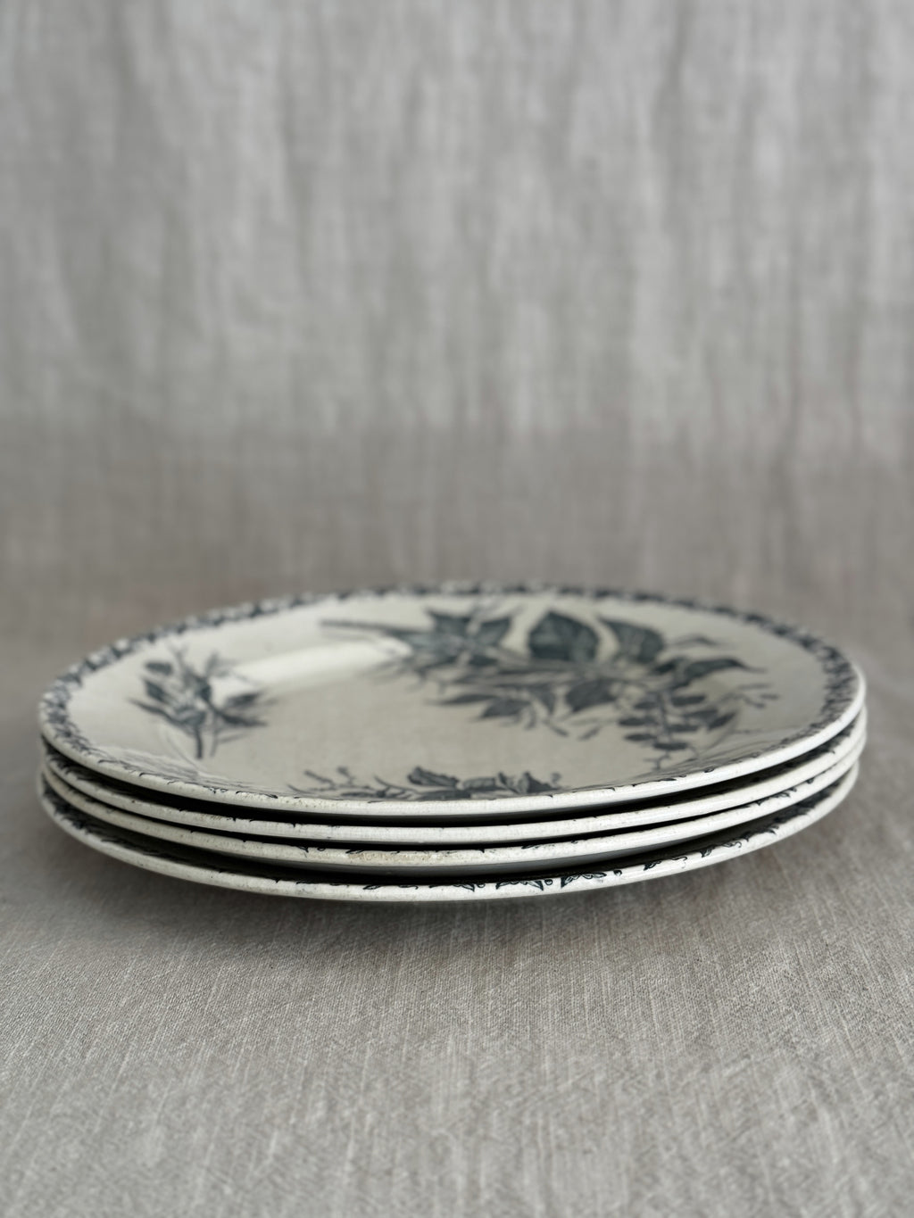Stack of four cream terre de fer plates seen from the side, showing the thin rims and the green border print