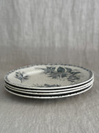 Stack of four cream terre de fer plates seen from the side, showing the thin rims and the green border print