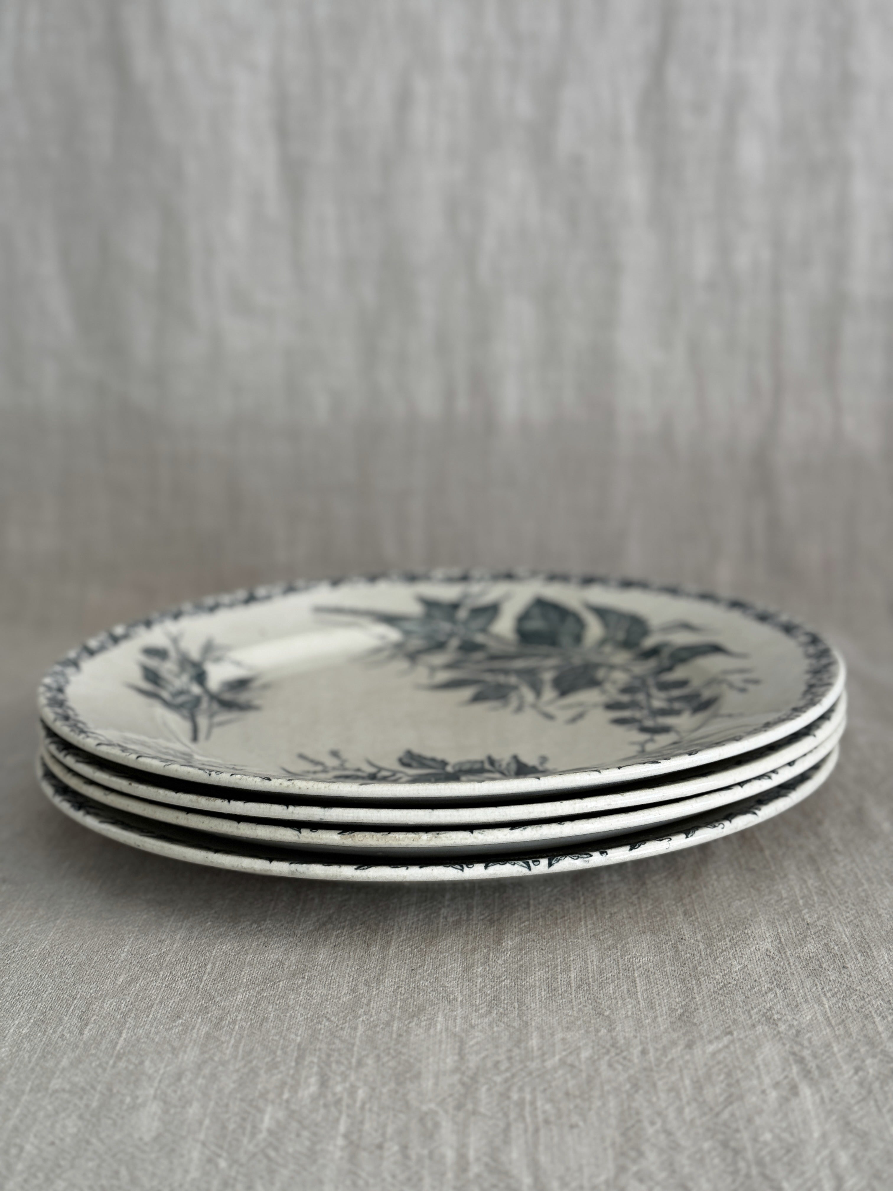 Stack of four cream terre de fer plates seen from the side, showing the thin rims and the green border print