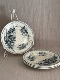 Four French green transferware luncheon plates in a blackberry pattern, one upright on a white iron plate stand and three stacked on a linen cloth